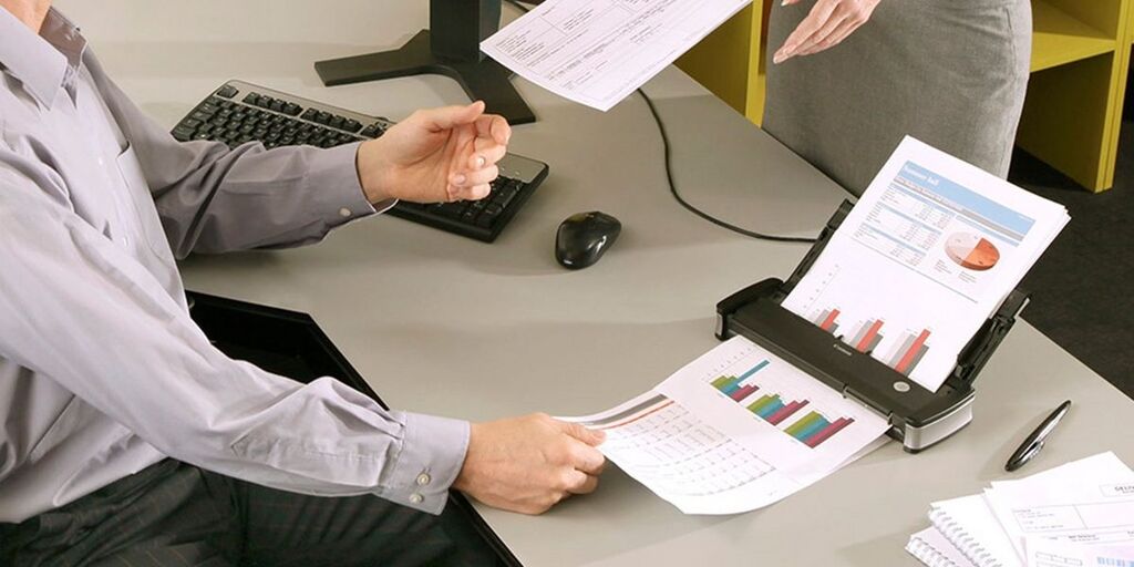 Medarbejder håndterer printede dokumenter og rapporter ved printer i kontormiljø