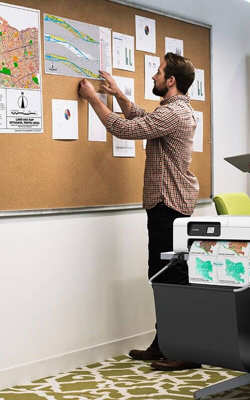 Medarbejder arbejder med ophængte dokumenter og analyser på opslagstavle i kontormiljø